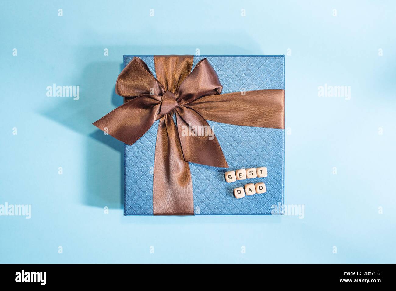 Un regalo blu con striscia marrone su sfondo blu. Un segno migliore papà per felice festa del Padre da blocchi di legno. Concetto di festa del Padre. Foto Stock