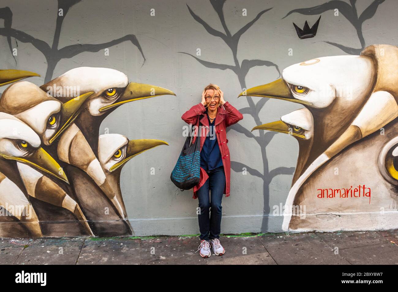Attacco di becco e fobia degli uccelli a Londra. Una giovane donna di fronte a un murale di pinguini che la minacciano con le loro perle. Il dipinto è firmato dall'artista Anamarietta. Street Art in Royal Borough di Kensington e Chelsea, Inghilterra Foto Stock