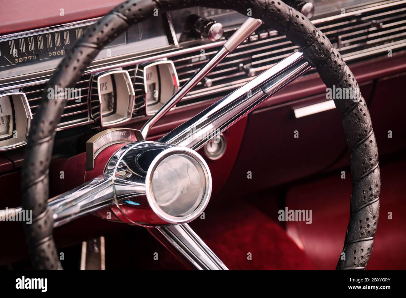Volante, quadranti e manopole sul cruscotto e pannello anteriore in pelle rosso rubino di lusso oldtimer Foto Stock