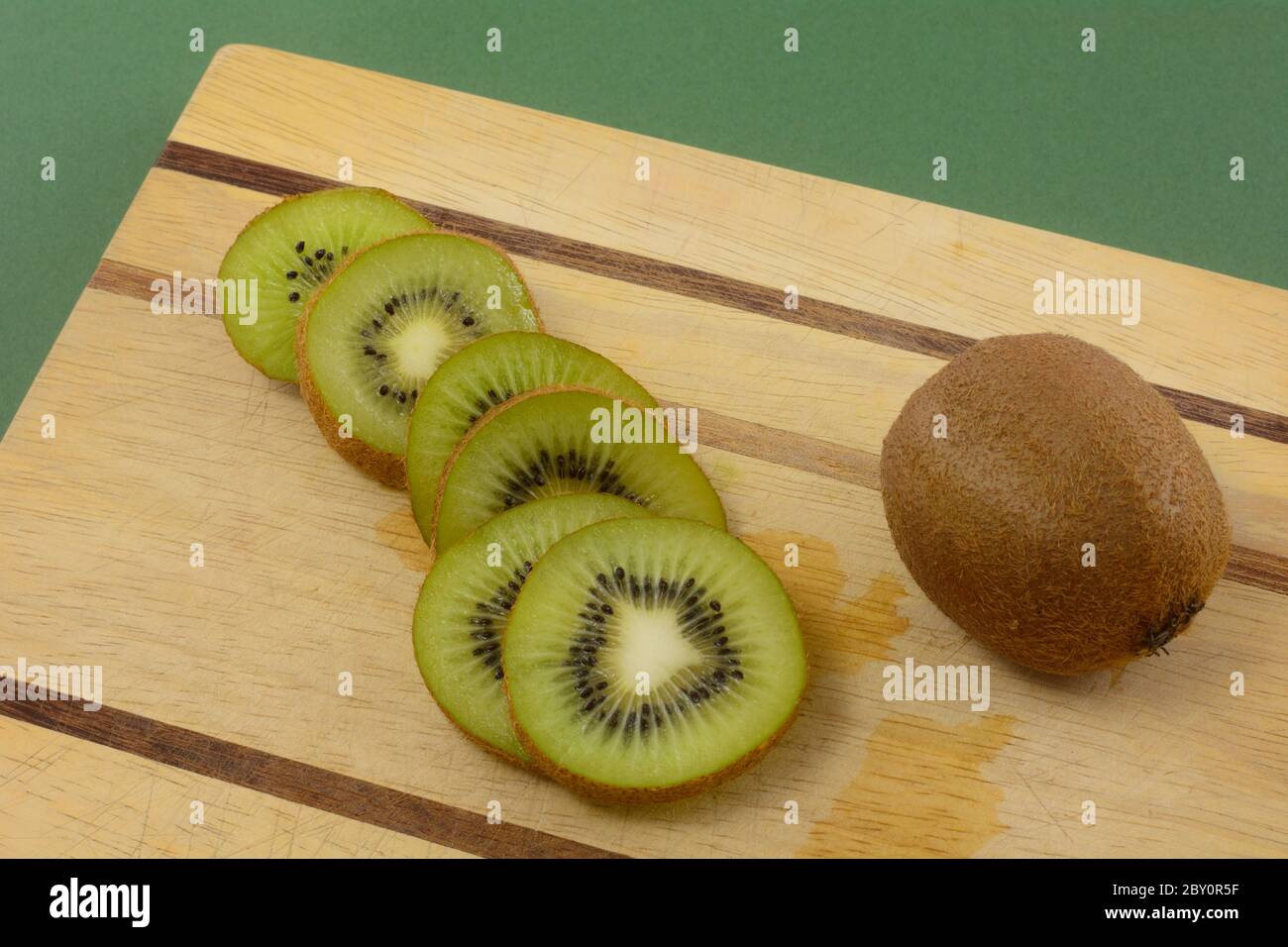 Fette di kiwi e frutta intera kiwi su tagliere di legno su sfondo verde Foto Stock