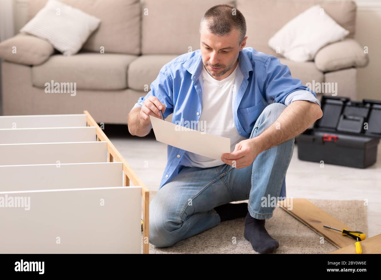 Uomo che monta il cabinet seduto leggere le istruzioni di installazione a casa Foto Stock