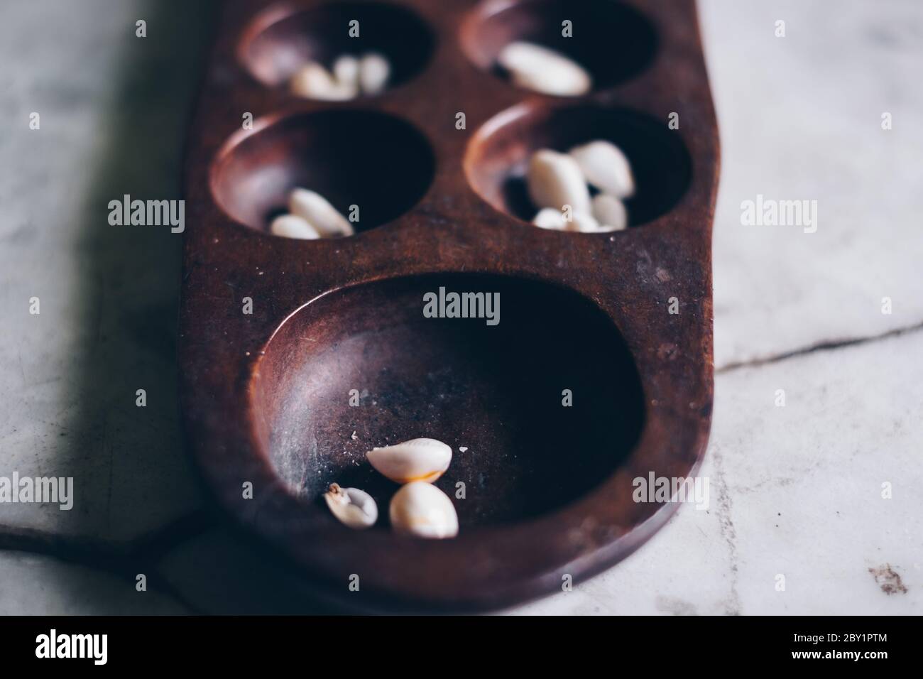 Primo piano della parte di testa di Sungka, gioco di mancala filippina, su un tavolo di marmo bianco con pezzi di conchiglie. Messa a fuoco selettiva. Foto Stock