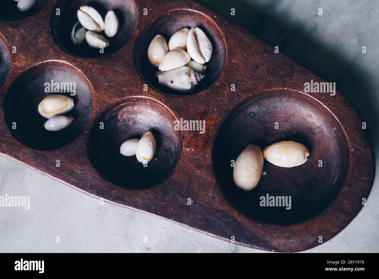 Primo piano della parte di testa di Sungka, gioco di mancala filippina, su un tavolo di marmo bianco con pezzi di conchiglie. Messa a fuoco selettiva. Foto Stock