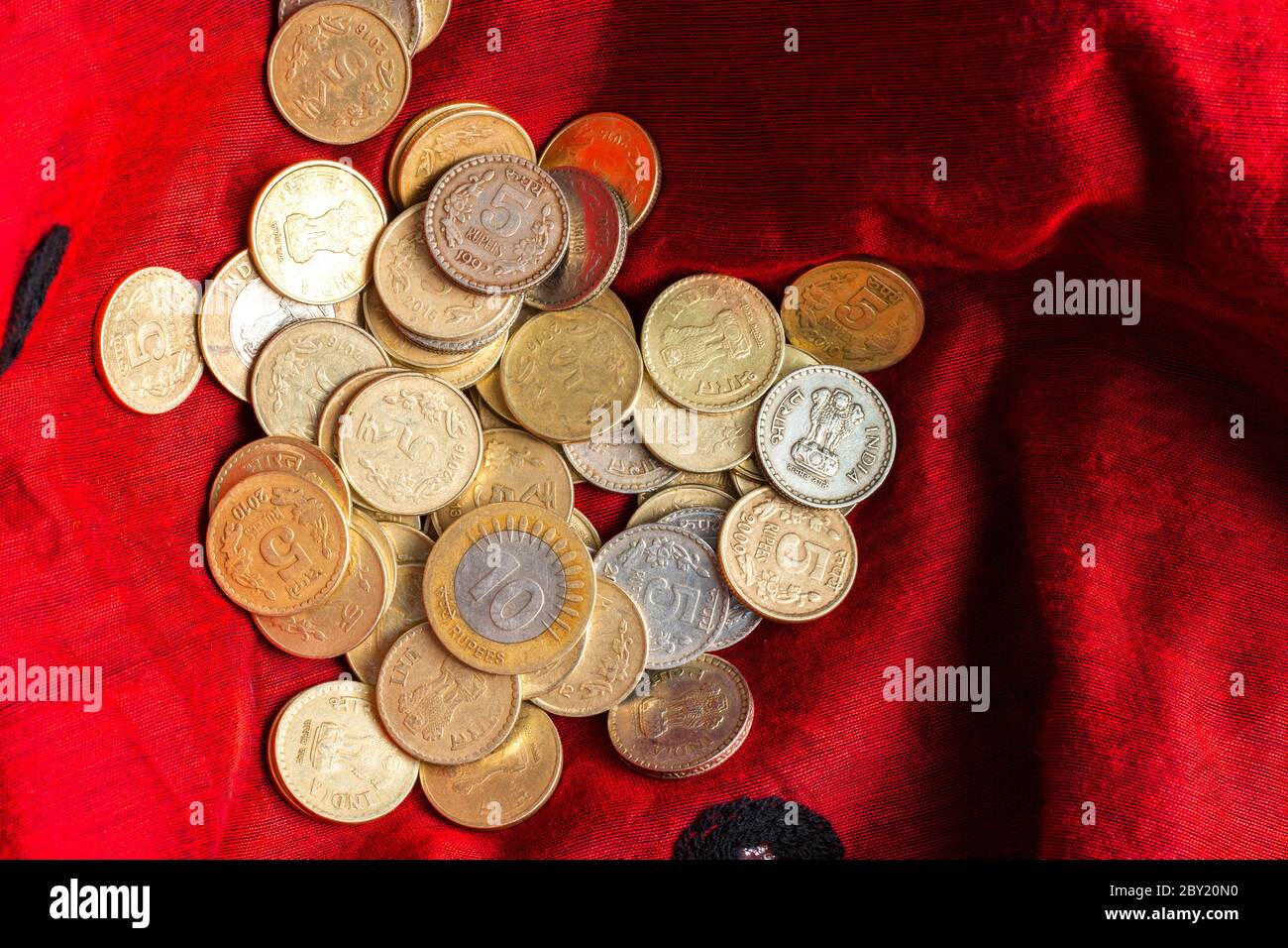 Monete indiane di cinque e dieci rupie sono tenute in un panno rosso Foto Stock