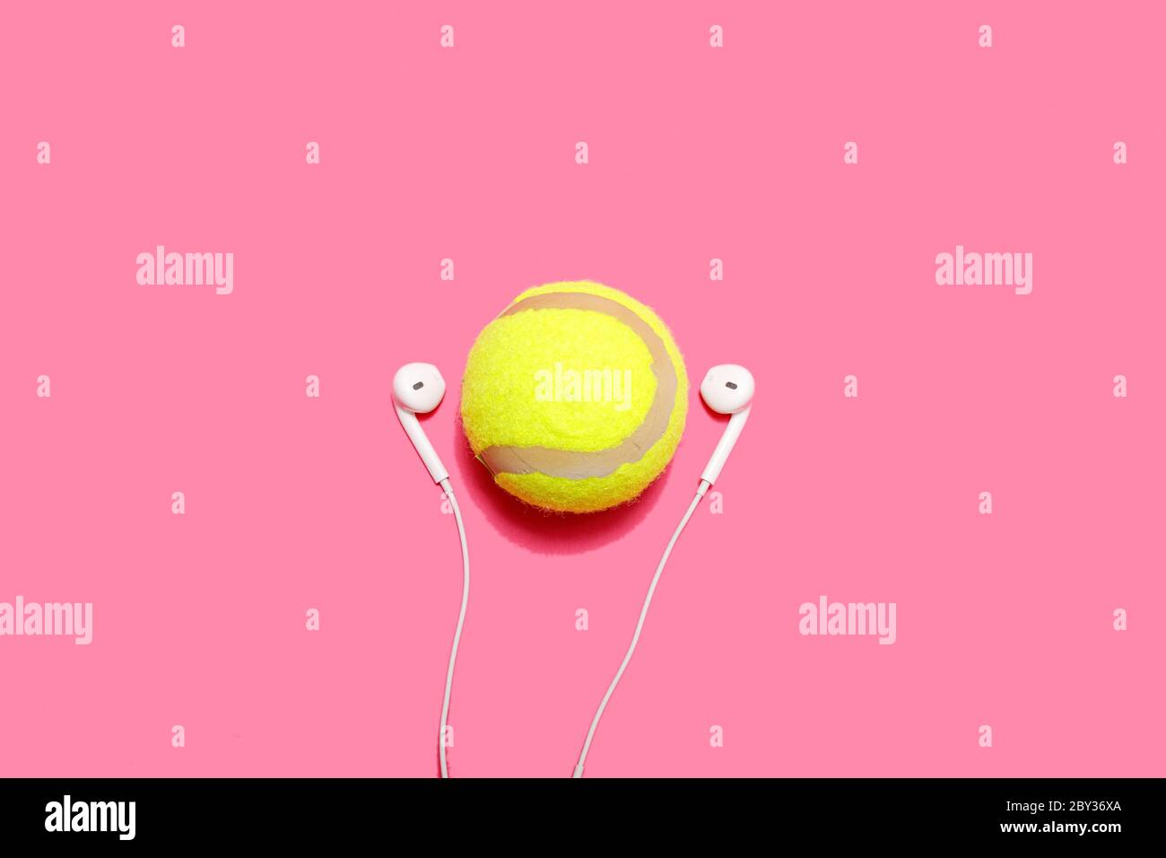 Palla da tennis e auricolari su sfondo rosa pastello. Entra nello sport e goditi la musica. Concetto minimo di sport. Spazio di copia per il testo. Foto Stock