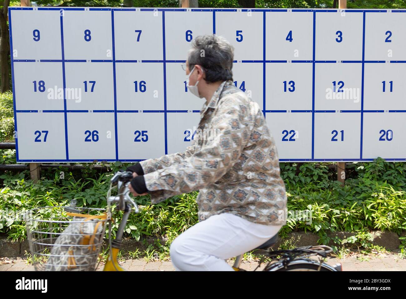 Una donna che indossa una maschera facciale in bicicletta passa accanto a una bacheca eretta appositamente per i poster dei candidati per le prossime elezioni gubernatorial di Tokyo il 5 luglio il 9 giugno 2020, Tokyo, Giappone. Il periodo della campagna inizia ufficialmente il 18 giugno. Credit: Rondrigo Reyes Marin/AFLO/Alamy Live News Foto Stock