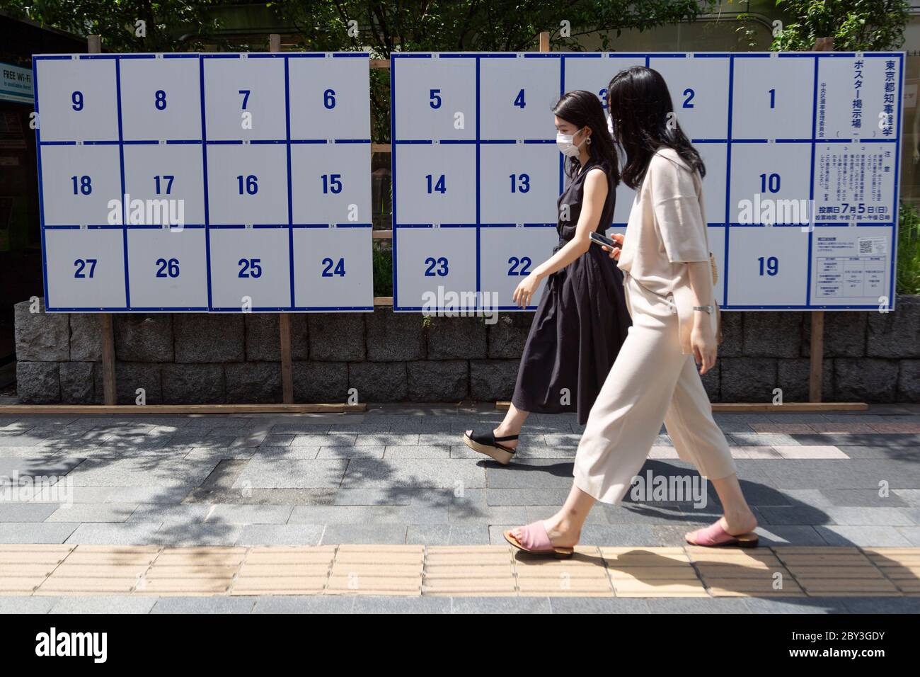 I pedoni che indossano maschere facciali passano davanti a una bacheca eretta appositamente per i poster dei candidati per le prossime elezioni gubernatorial di Tokyo il 5 luglio, il 9 giugno 2020, Tokyo, Giappone. Il periodo della campagna inizia ufficialmente il 18 giugno. Credit: Rondrigo Reyes Marin/AFLO/Alamy Live News Foto Stock