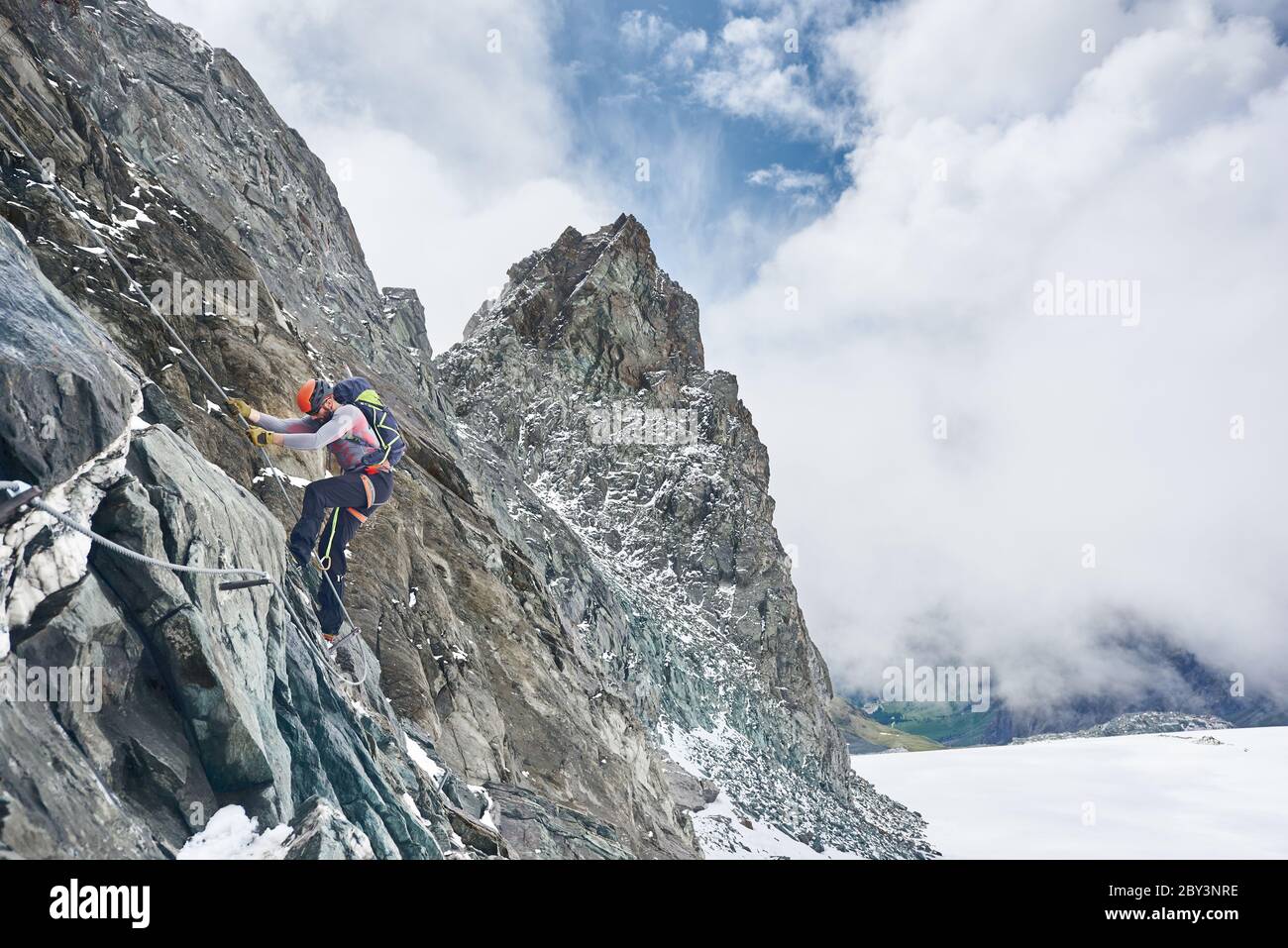 Scalatore in casco di sicurezza con corda fissa mentre sale montagna rocciosa. Alpinista maschile con formazione naturale di roccia di arrampicata zaino. Concetto di alpinismo e alpinismo invernale. Foto Stock