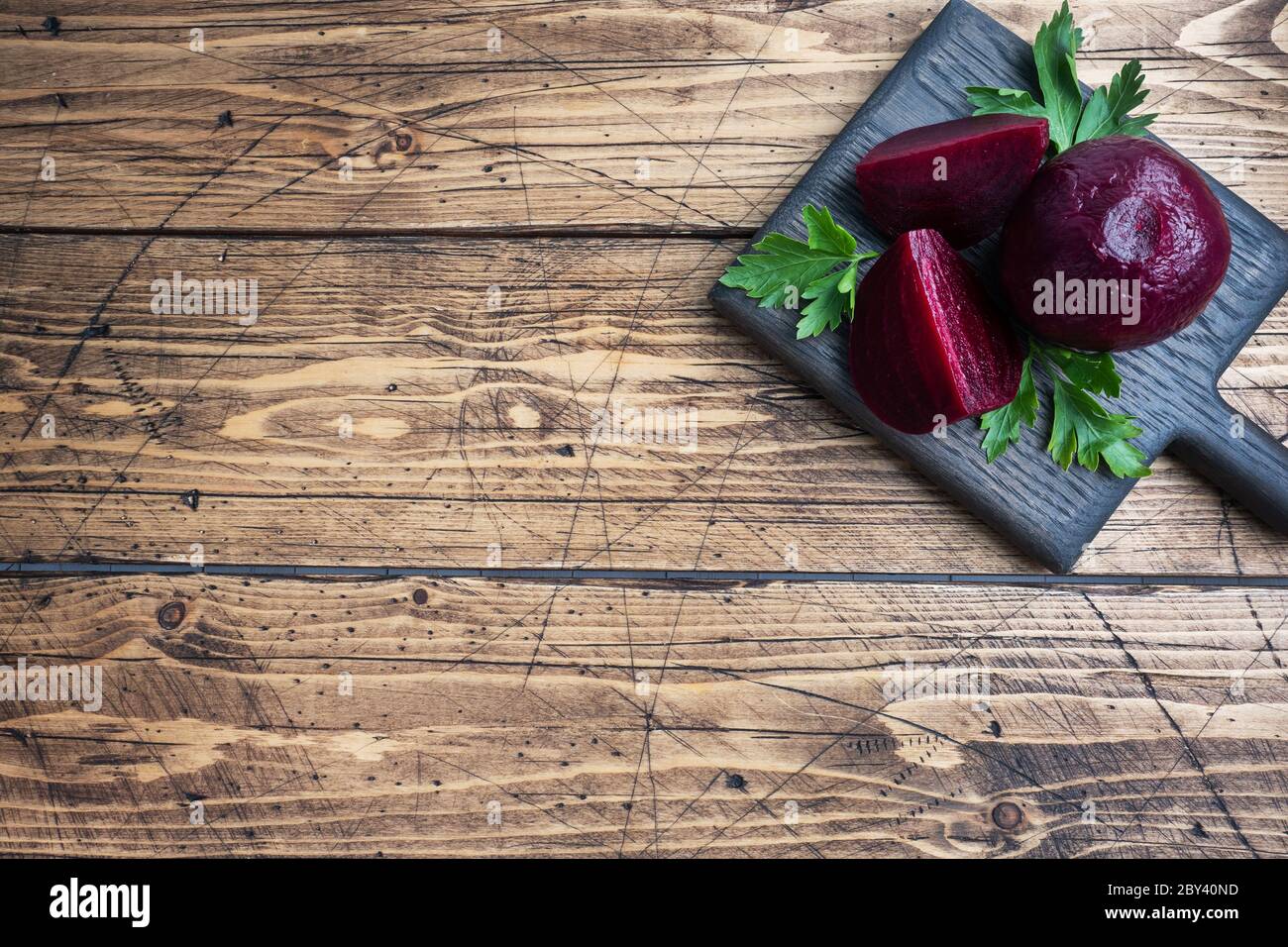 Barbabietole bollite intere e tagliate su un tagliere con foglie di prezzemolo su uno sfondo rustico di legno Copia spazio Foto Stock