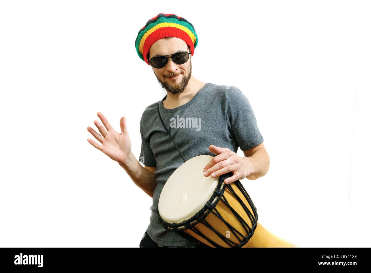 Giovane uomo caucasico in cappello rasta, occhiali da sole e t-shirt grigia  su sfondo bianco giocano sul tamburo africano djembe Foto stock - Alamy