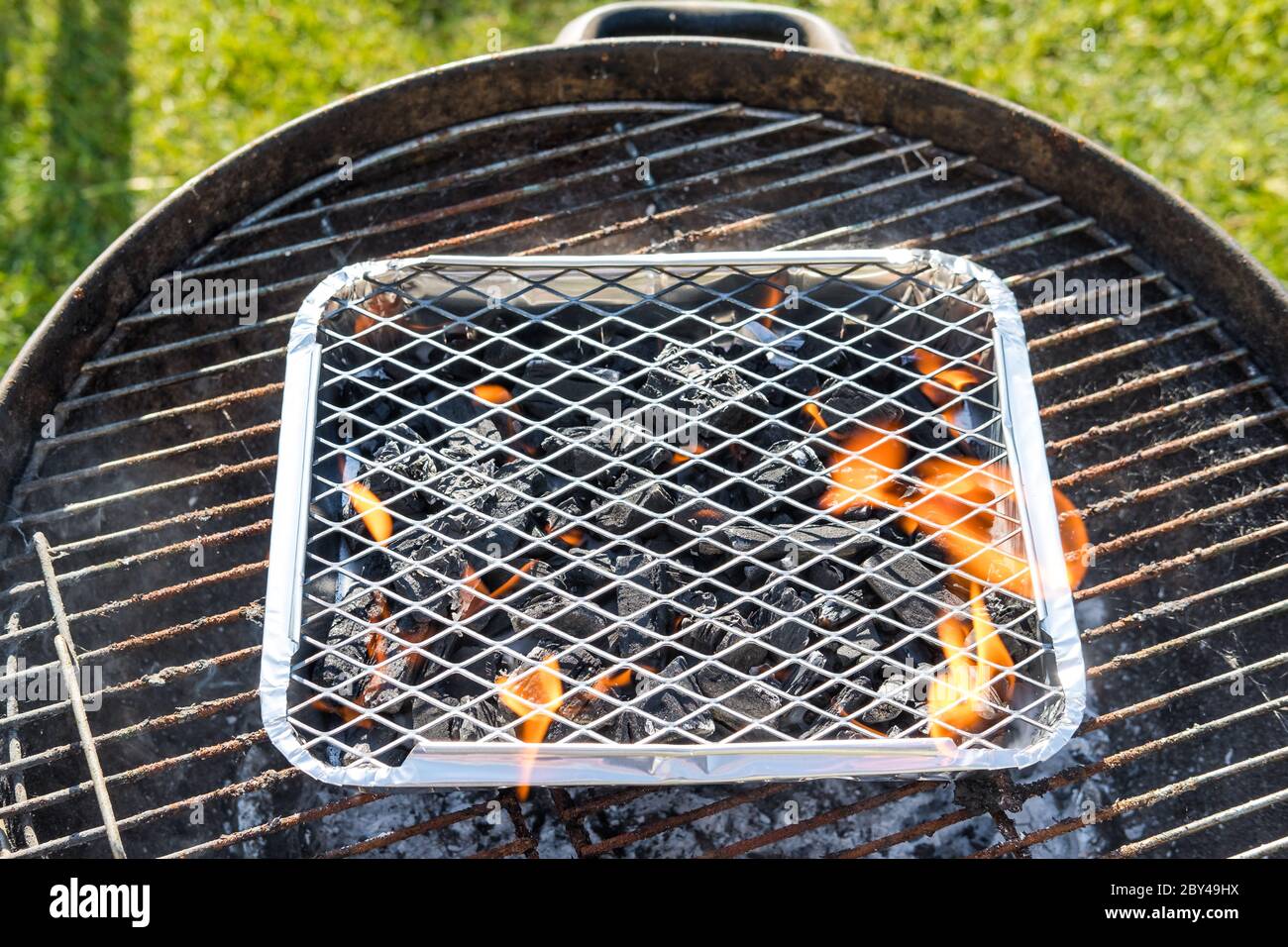 Fuoco superficiale di un barbecue di campeggio visto in un barbecue di dimensioni complete. Si vedono le fiamme emesse, pronte per la cottura della carne. Visto in un grande giardino. Foto Stock