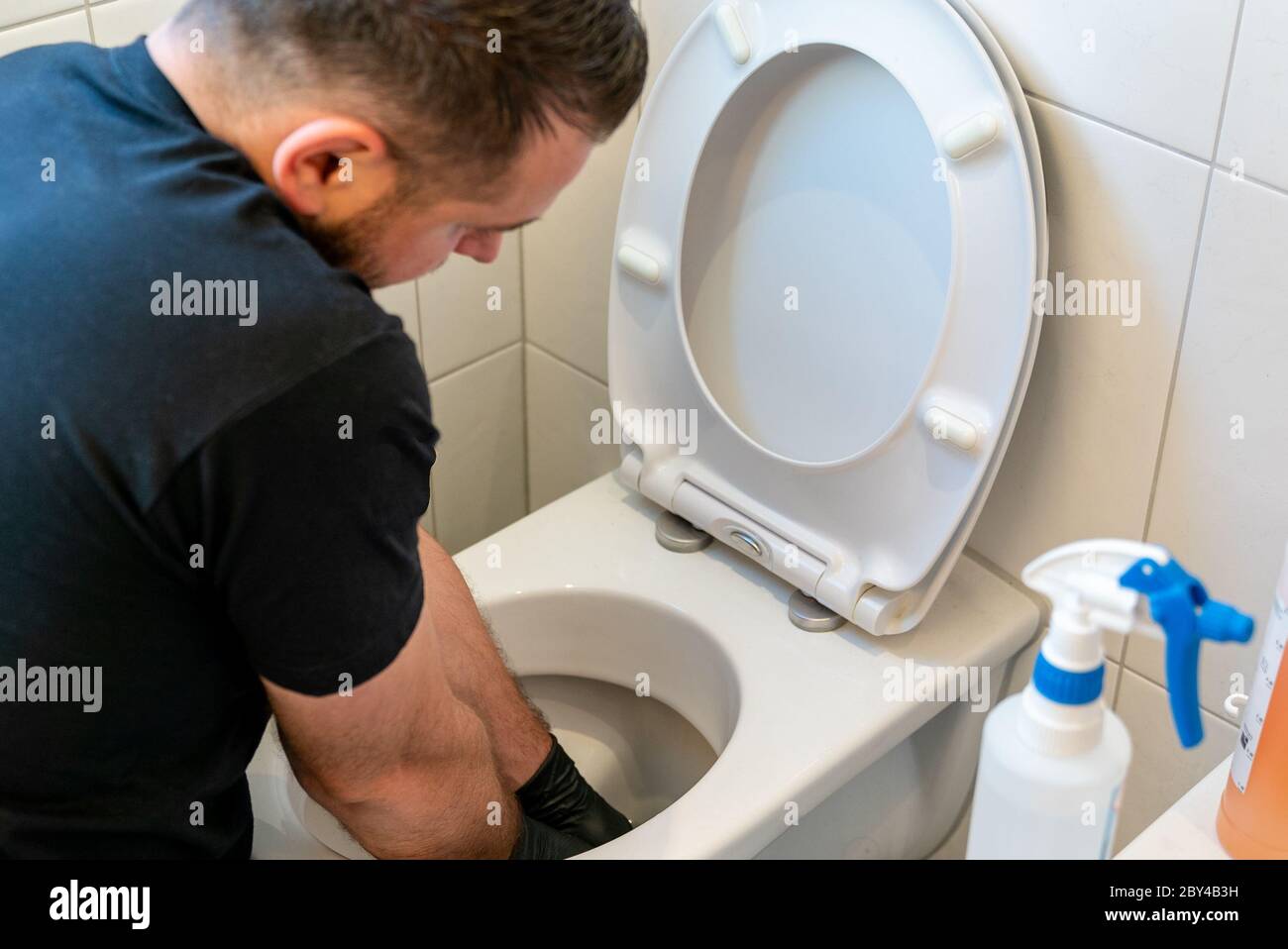 Un pulitore professionale pulisce molto accuratamente un gabinetto in ceramica in un bagno moderno Foto Stock