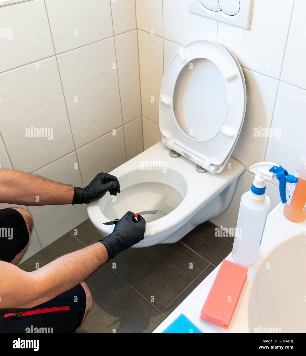 Un pulitore professionale pulisce molto accuratamente un gabinetto in ceramica in un bagno moderno Foto Stock