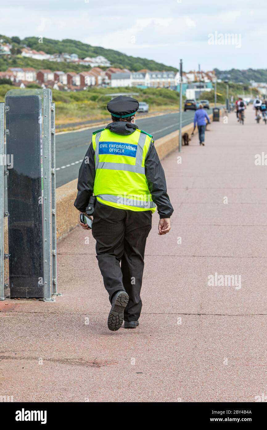 Un ufficiale dell'Enforcement civile che cammina lungo una passeggiata sul lungomare durante il blocco del coronavirus Foto Stock