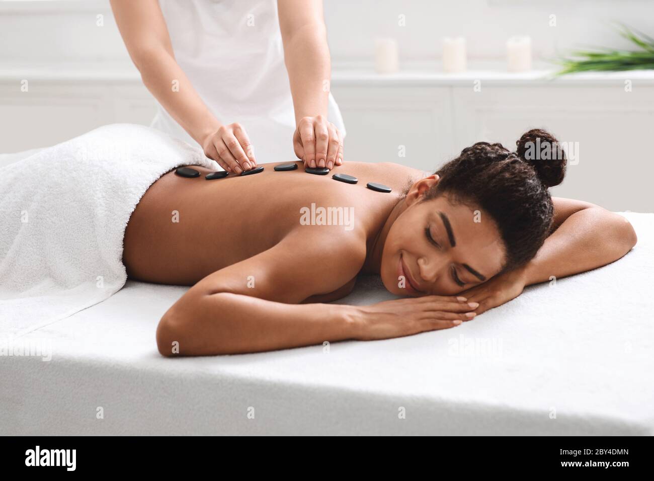 Rilassante donna africana che ottiene massaggio di pietra calda alla spa Foto Stock