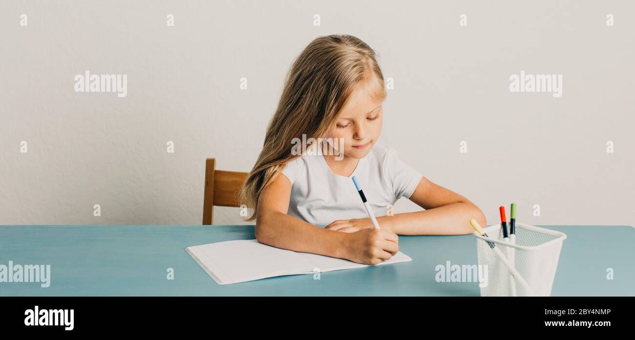bionda ragazza si siede a un tavolo e scrive in un notebook Foto Stock