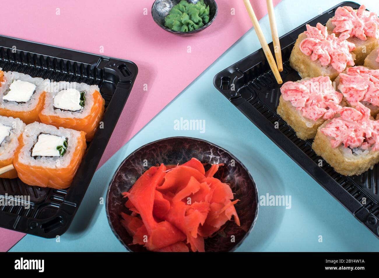 Set di sushi assortiti serviti in scatole di plastica. Philadelphia e lava Rolls. Consegna di cibo. Sfondo rosa e blu Foto Stock