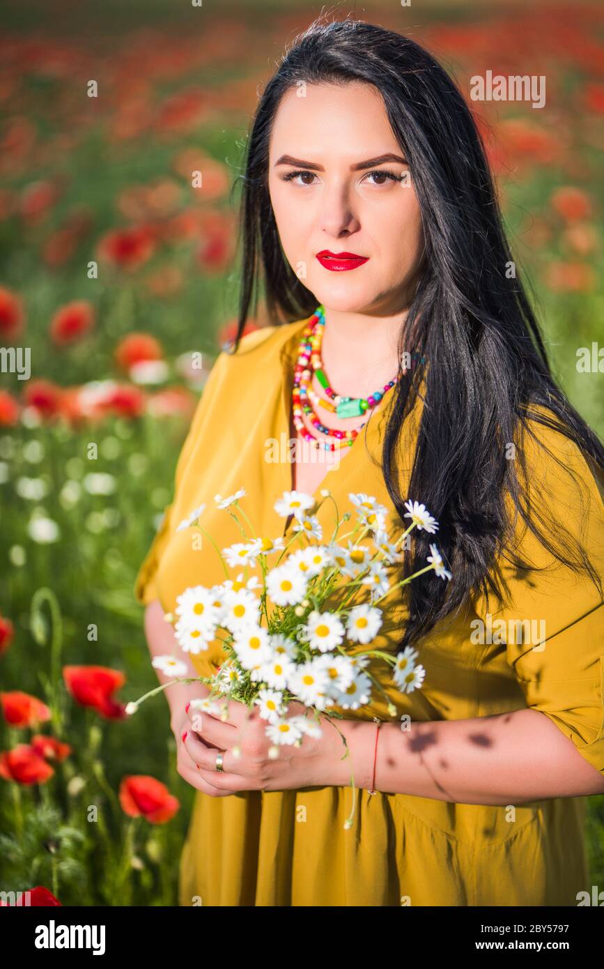 Ritratto di una bella giovane donna in una blusa gialla nel mezzo di un  campo di papavero che tiene in mano un bouquet di fiori bianchi Foto stock  - Alamy