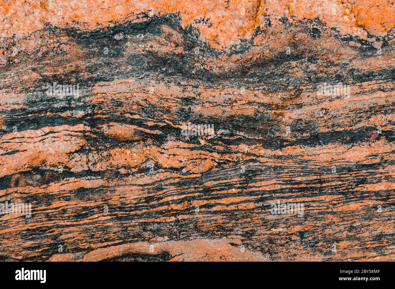 Tessitura ondulata di pietra granitica rossa tinta e strisce scure Foto Stock
