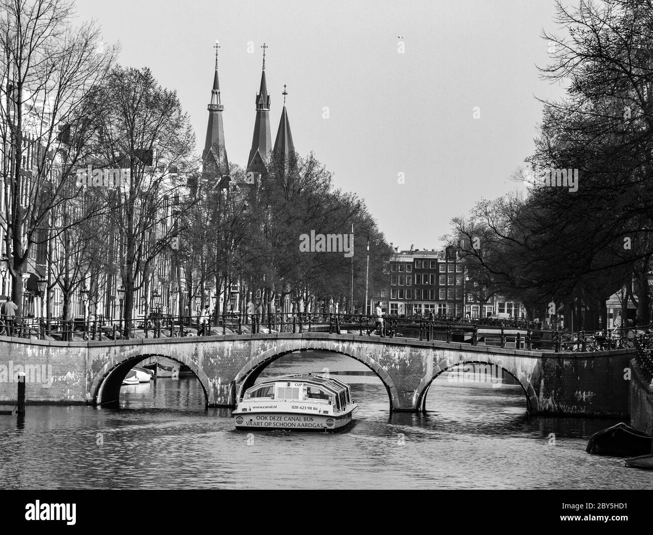 Gracht o Canal of Amsterdam con il tipico ponte basso e barca turistica nella prima primavera, Paesi Bassi. Immagine in bianco e nero. Foto Stock