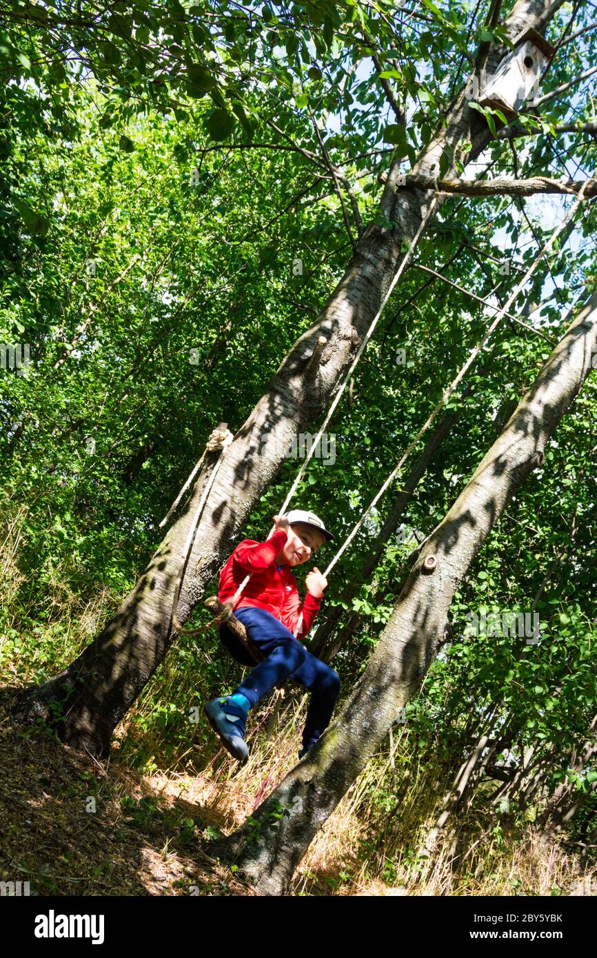 Ragazzo bambino bambino che gioca su swing appeso sugli alberi in giardino in primavera Foto Stock