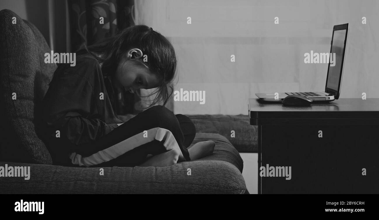 Infelice ragazza carina di bambini seduta sul divano vicino al computer e giocare in giochi mobili a casa. Ritratto di primo piano. Bianco e nero. Ombra scura Foto Stock