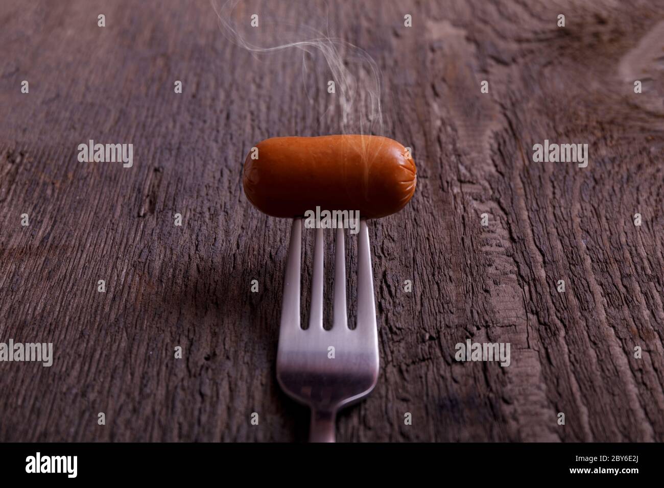 Salsiccia con fumo. Salsiccia bollita bollita su una forchetta con l'effetto del vapore su tavola di legno vintage. Foto Stock