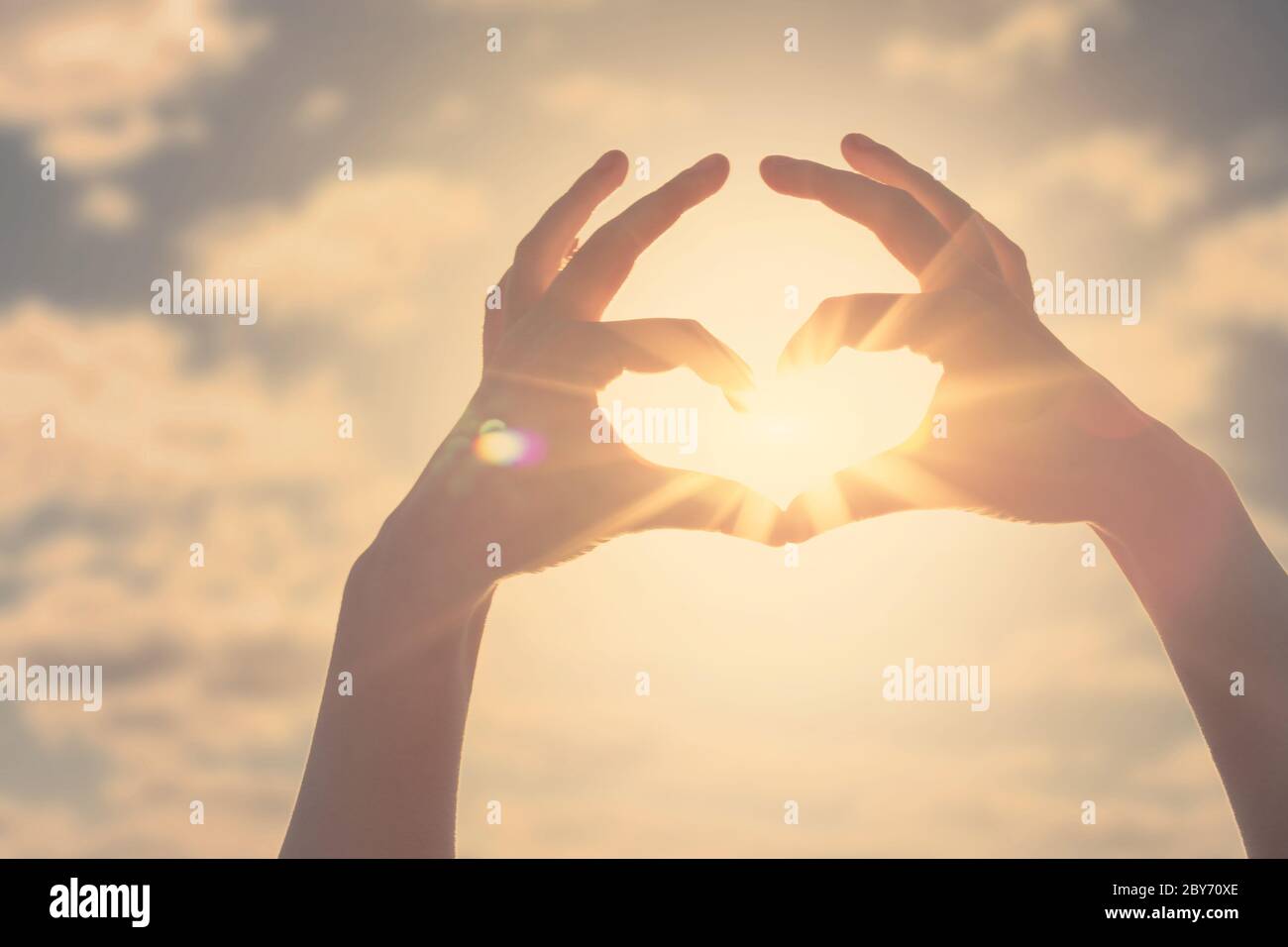 Silhouette a forma di cuore a mano realizzata contro il sole e il cielo di un'alba o tramonto. Concetto di libertà e amore. Foto Stock