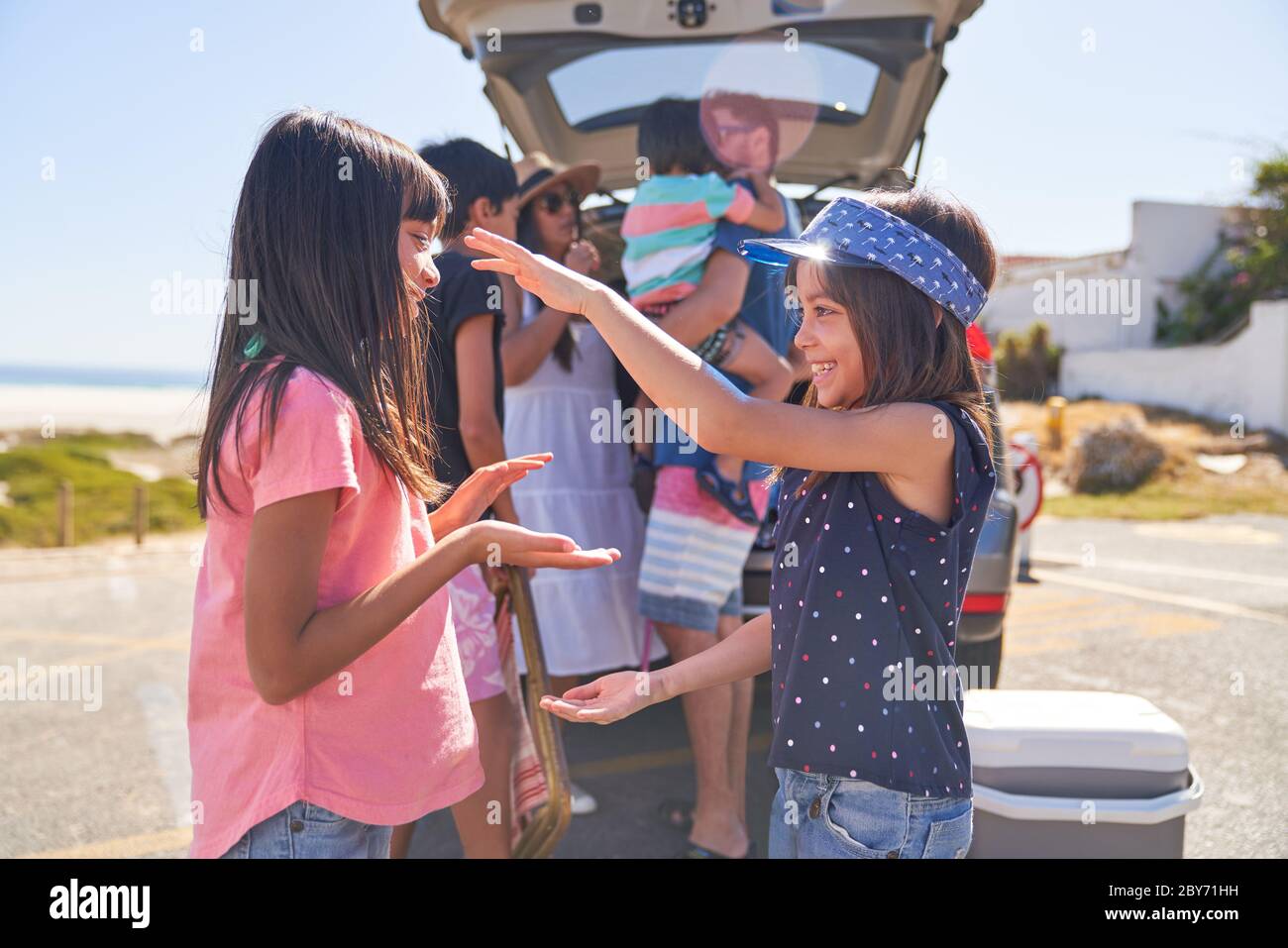 Sorelle felici che giocano a un gioco di batticuore nel parcheggio soleggiato della spiaggia Foto Stock