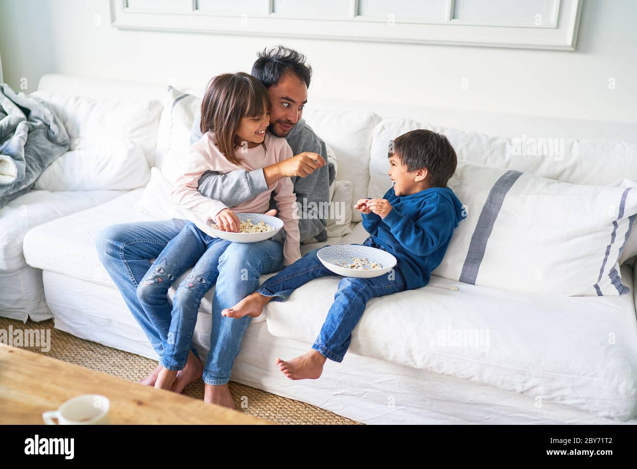 Padre e bambini mangiano popcorn sul divano del soggiorno Foto Stock