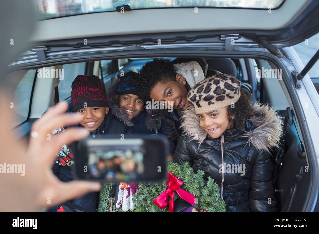 Felice famiglia con corona di Natale in posa per foto in auto Foto Stock