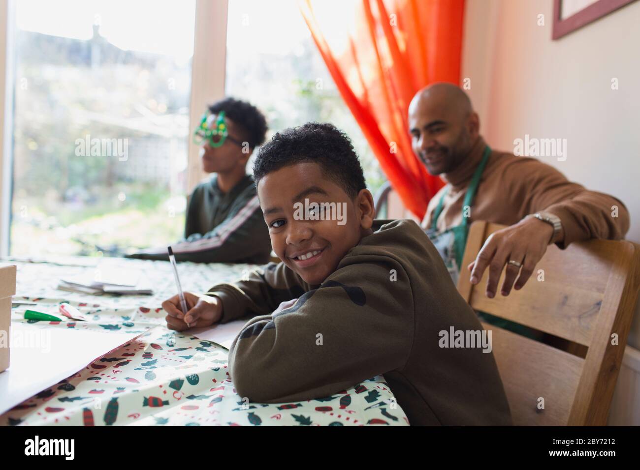 Ritratto ragazzo felice che scrive le schede di Natale al tavolo Foto Stock