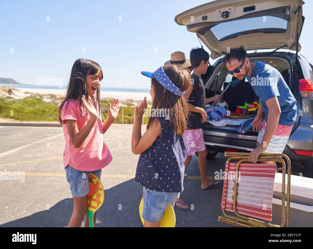 Sorelle felici che giocano a un gioco di batticuore nel parcheggio della spiaggia soleggiata Foto Stock