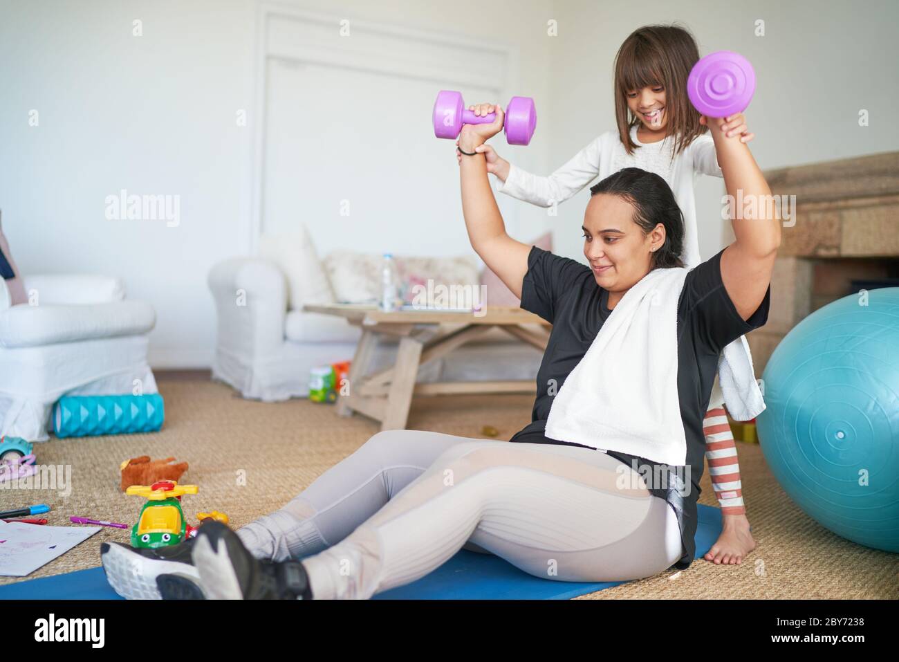 Figlia che aiuta la madre ad esercitarsi con i manubri nel soggiorno Foto Stock