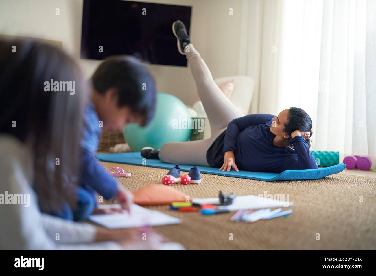 Madre che si esercita in soggiorno con bambini che si colorano nelle vicinanze Foto Stock