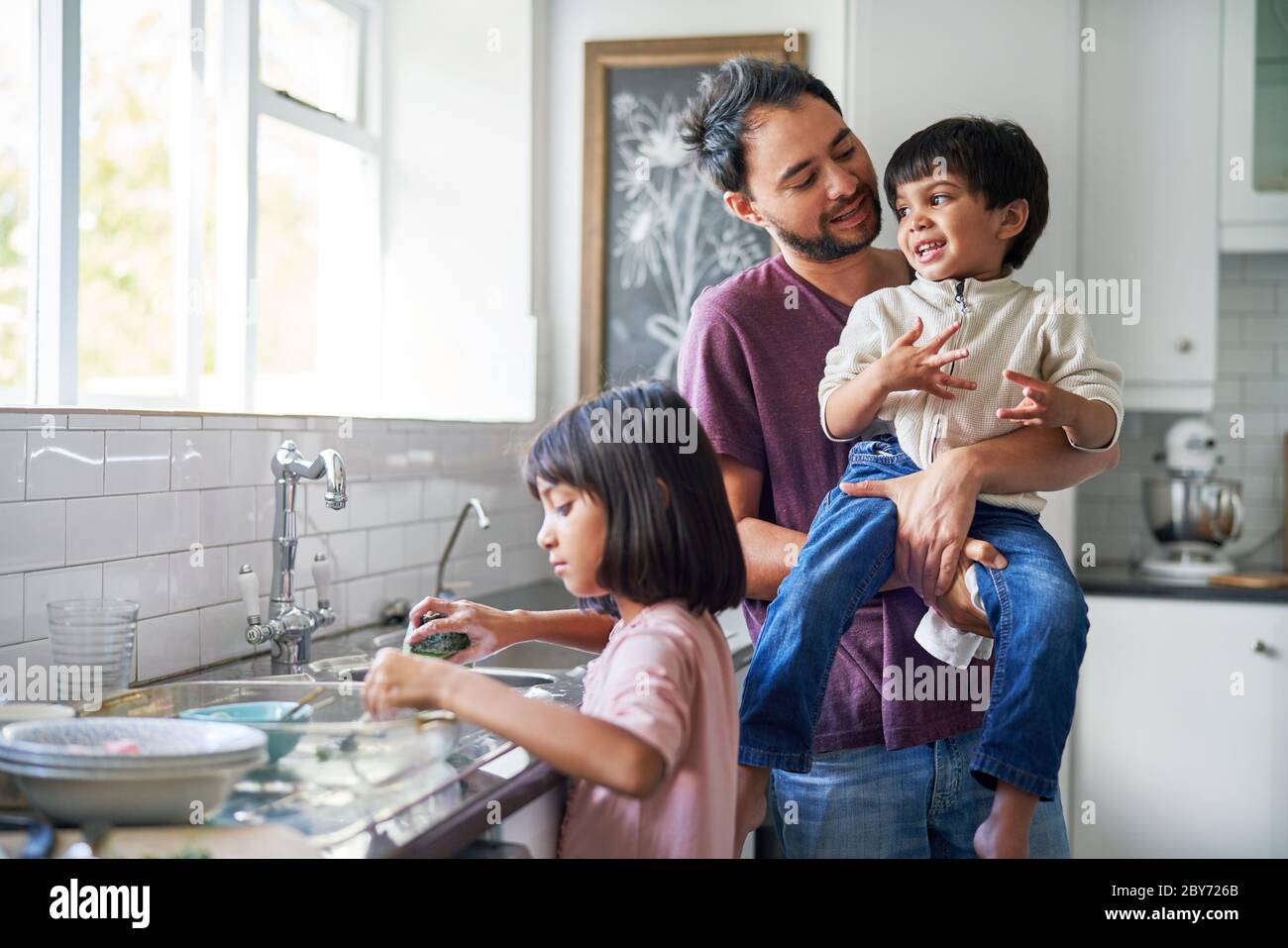 Buon padre e bambini che fanno piatti al lavello della cucina Foto Stock