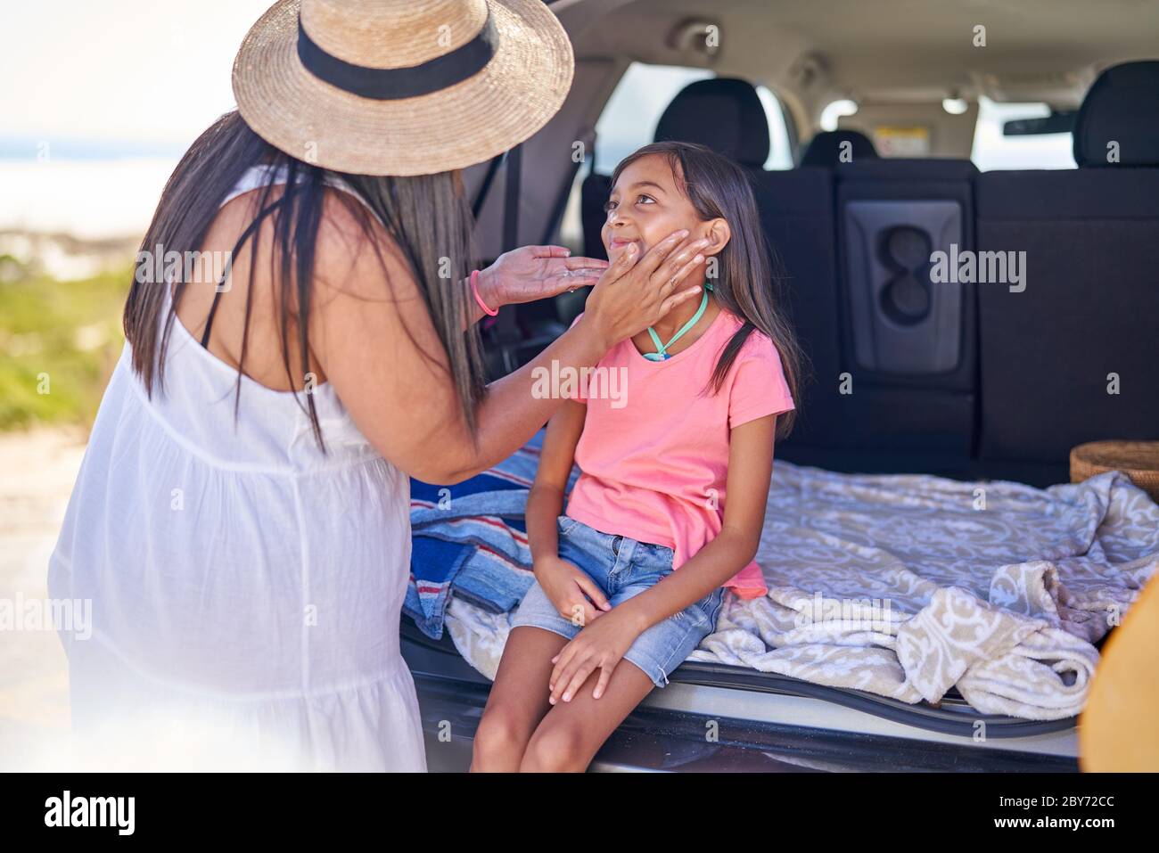 Madre affettuosa che applica la protezione solare alla figlia sul retro dell'automobile Foto Stock