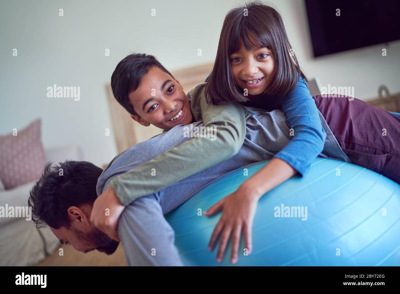 Ritratto giocoso bambini in cima al padre che si esercita sulla palla fitness Foto Stock