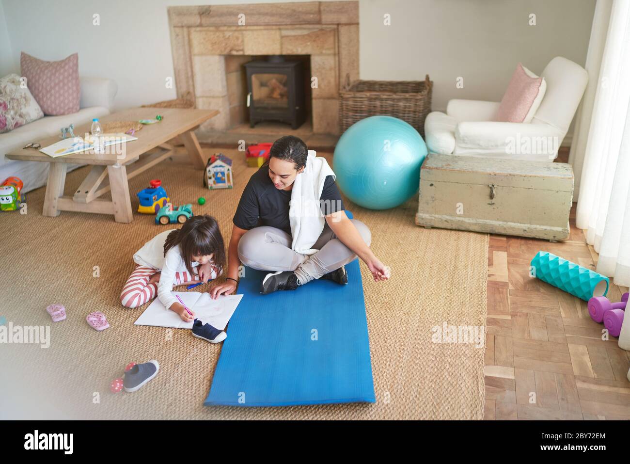 Madre su tappetino yoga guardando figlia colorazione sul pavimento del soggiorno Foto Stock