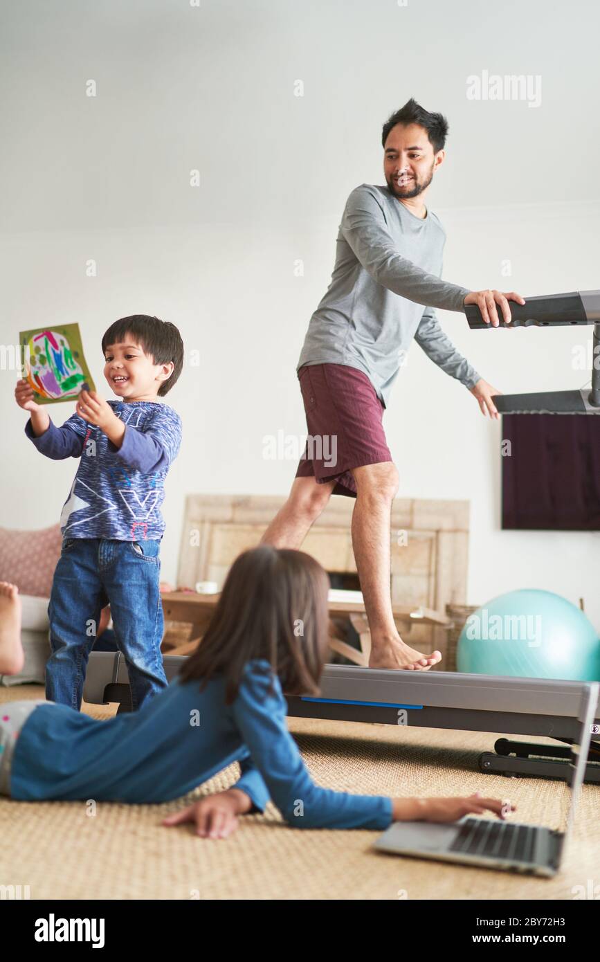 Padre che si esercita sul tapis roulant nel soggiorno con i bambini Foto Stock