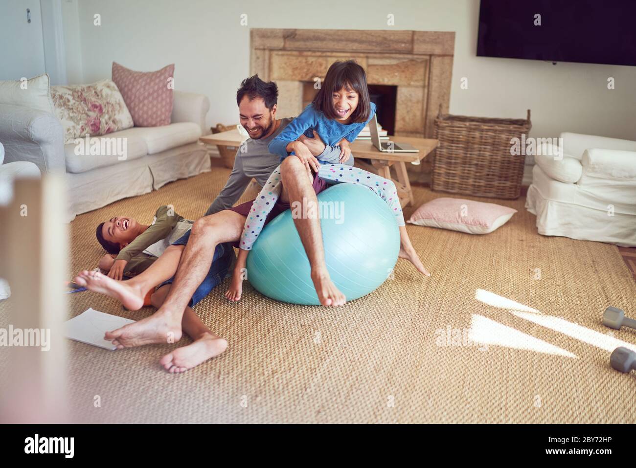 Un padre e dei bambini giocosi in una palla da fitness in soggiorno Foto Stock