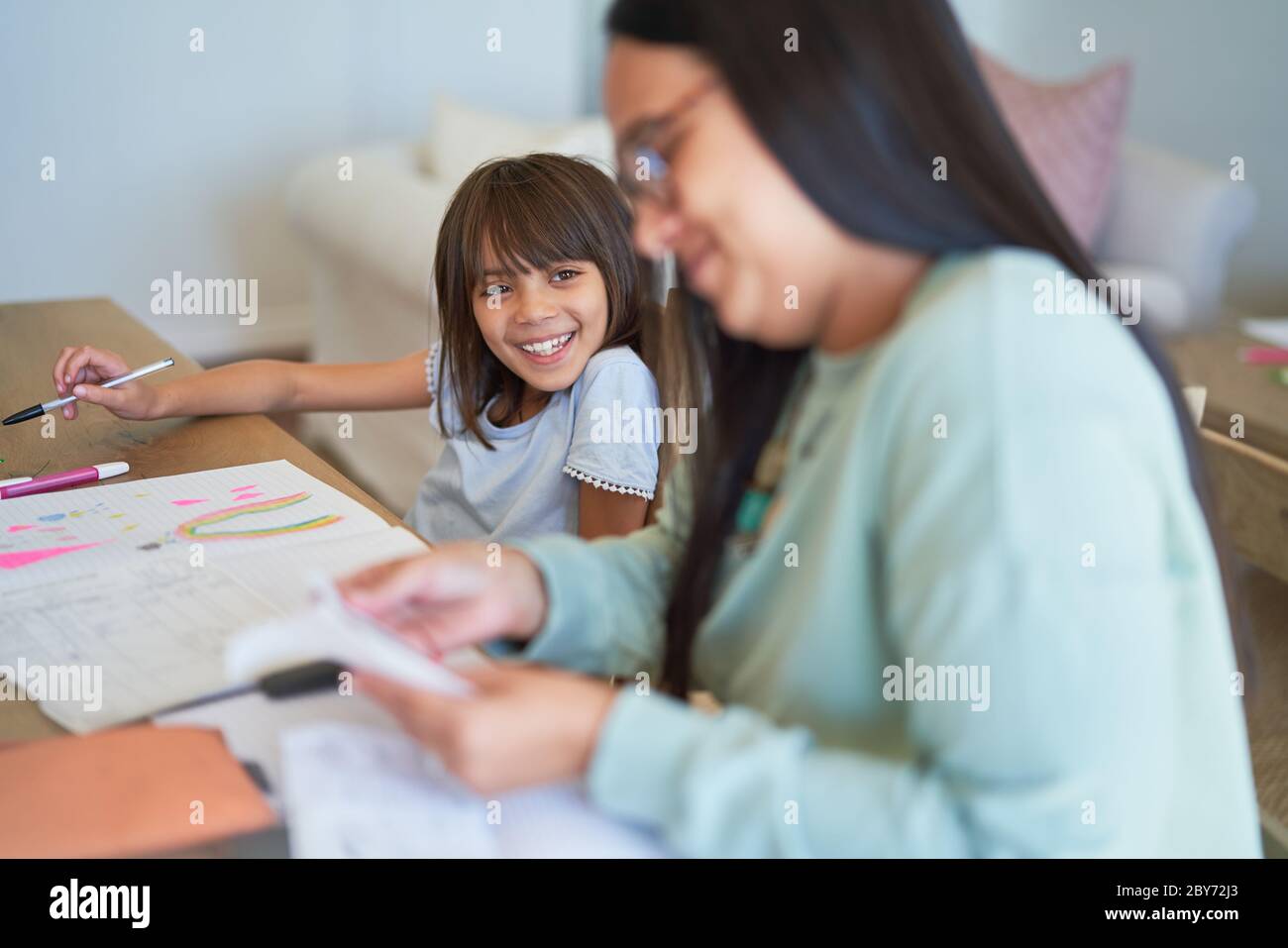 Felice ragazza colorazione accanto a madre pagando le fatture al tavolo da pranzo Foto Stock