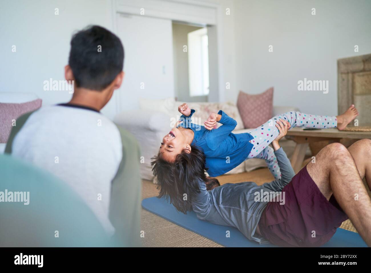 Il padre giocoso che solleva la figlia e che si esercita in soggiorno Foto Stock