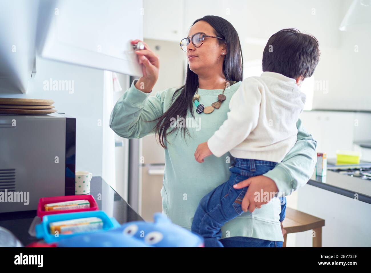 Madre che tiene il figlio e prepara i pranzi in cucina Foto Stock