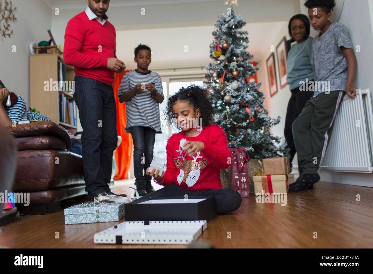 La famiglia che guarda la ragazza apre regali di Natale sul pavimento del soggiorno Foto Stock