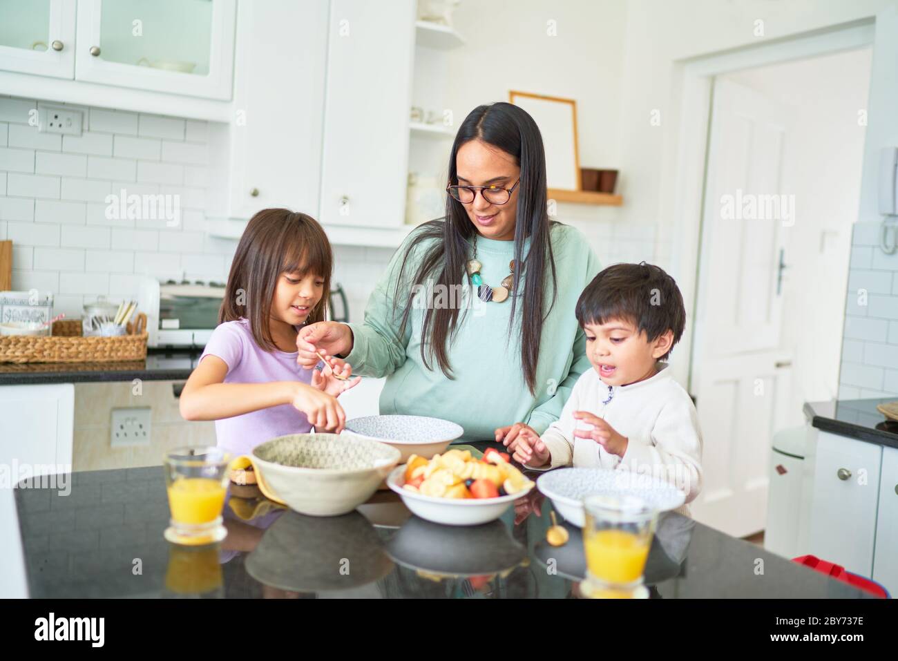 Madre e bambini preparano frutta in cucina Foto Stock