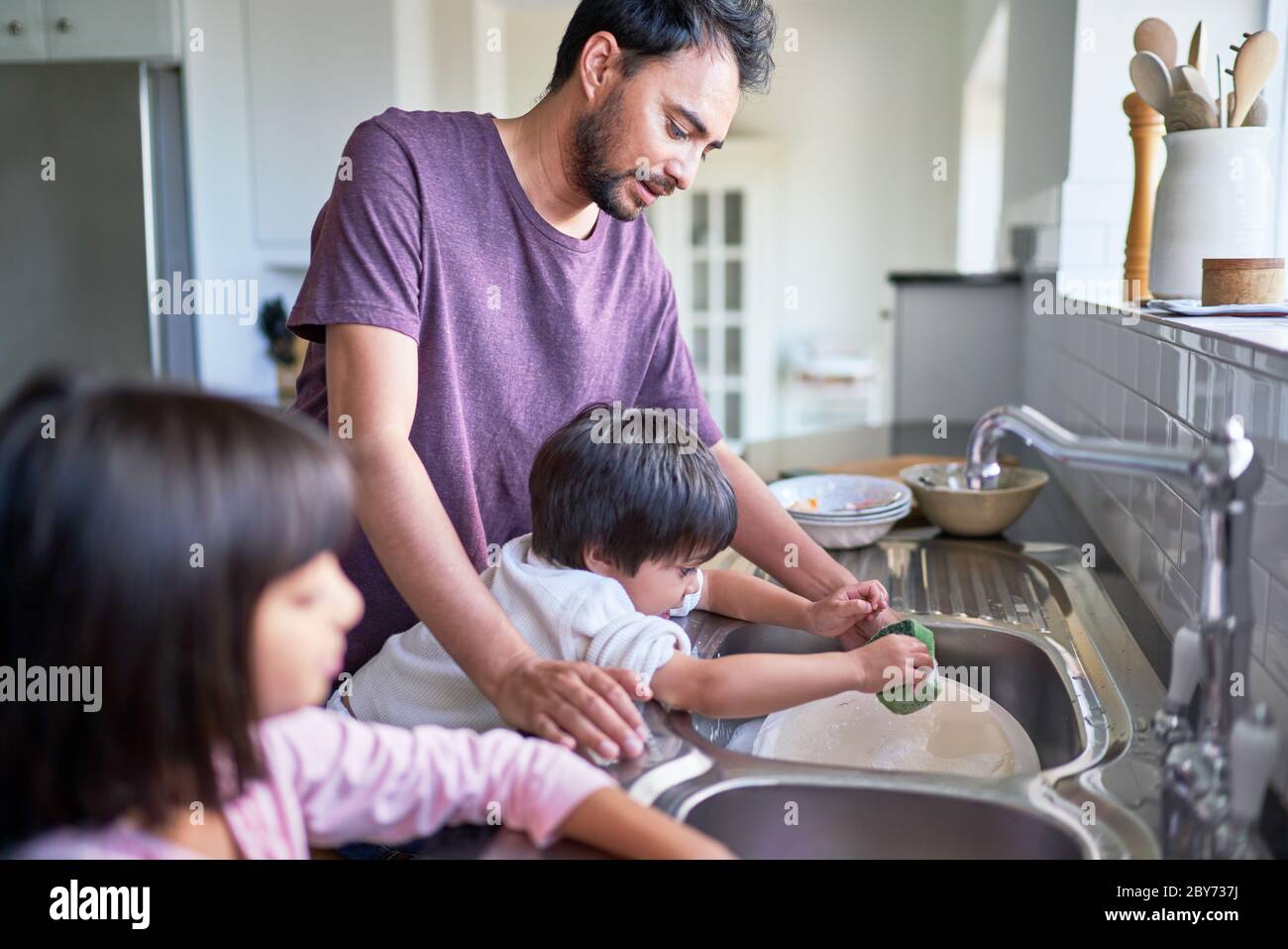 Padre e bambini che fanno piatti al lavello della cucina Foto Stock