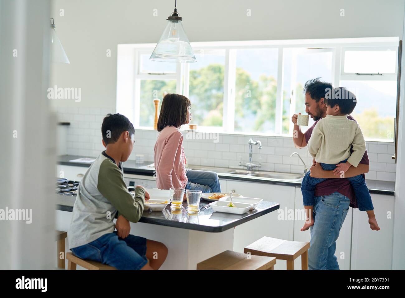 Padre e bambini mangiano cibo da asporto in cucina Foto Stock
