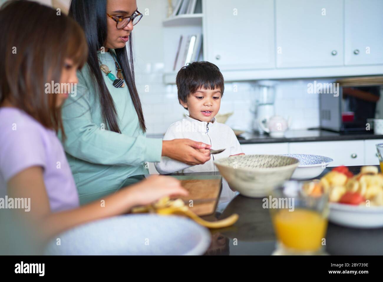 Madre e bambini tagliano frutta fresca in cucina Foto Stock