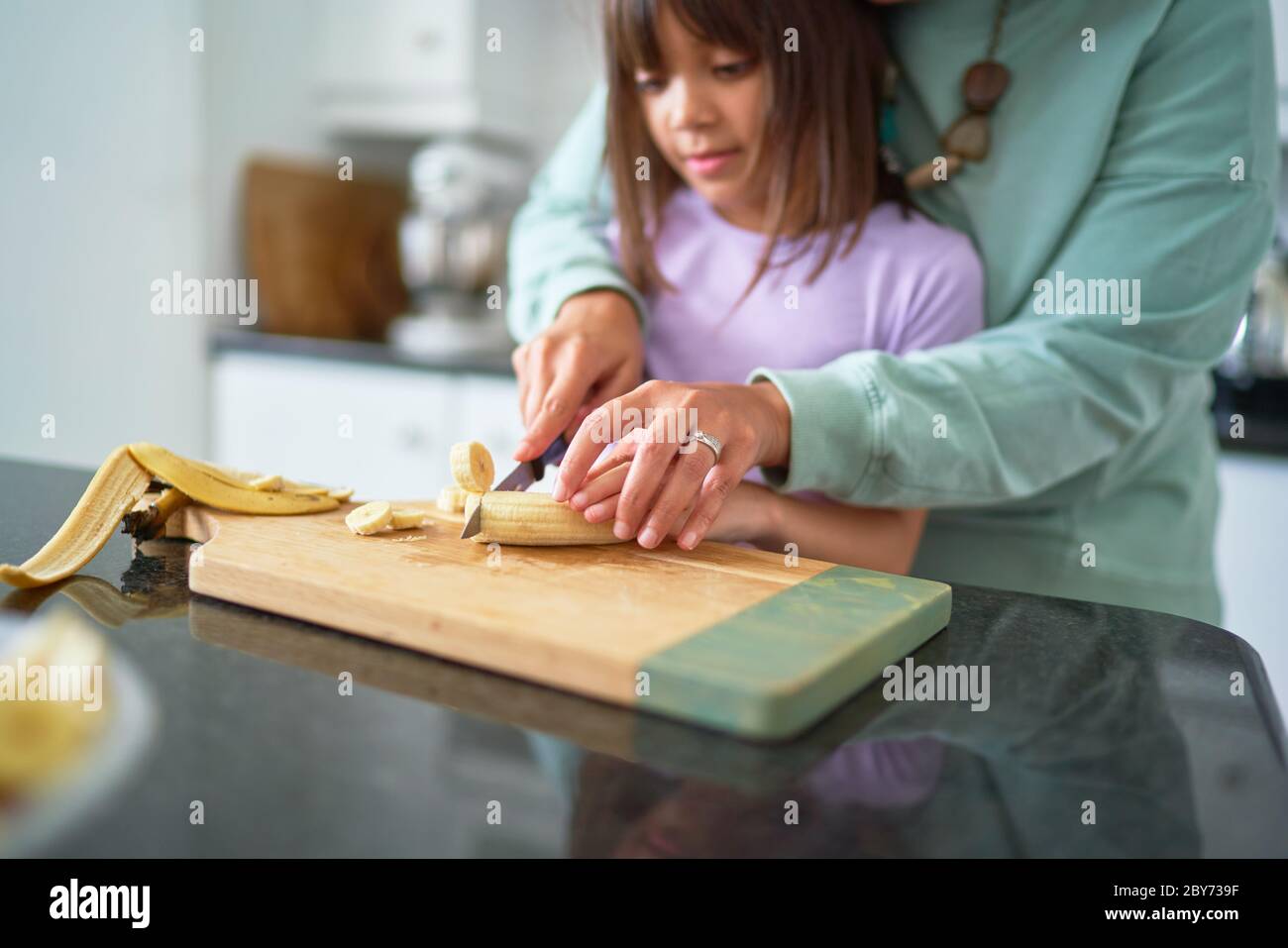 Madre che aiuta la figlia ha tagliato la banana in cucina Foto Stock
